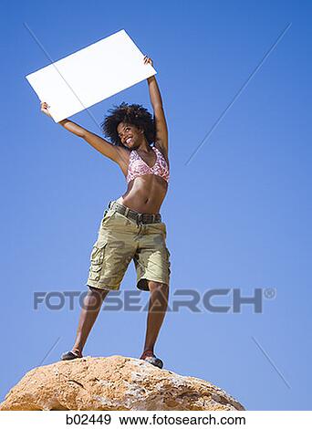 Low angle view of a young woman holding a blank sign View Large Photo Image Stock Photo - Low angle view of a young woman holding a blank sign. Fotosearch