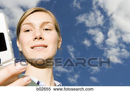 Low angle view of a young woman holding a mobile phone View Large Photo Image Stock Photography - Low angle view of a young woman holding a mobile phone. Fotosearch