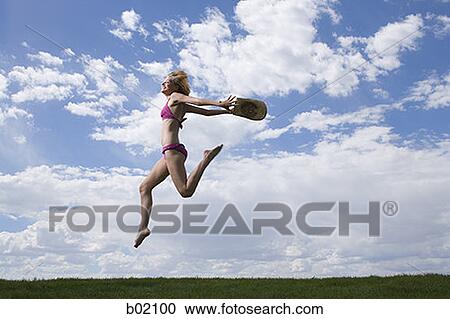 Stock Image - Low angle view of a young woman jumping. Fotosearch