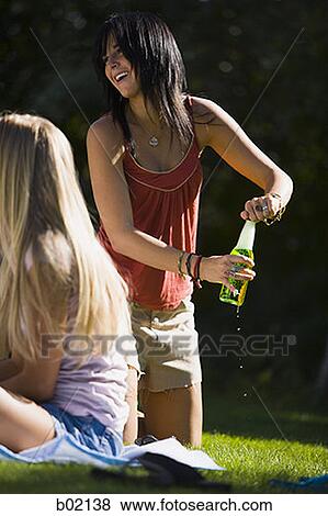 Stock Photo - Low angle view of a young woman opening a beer bottle. Fotosearch