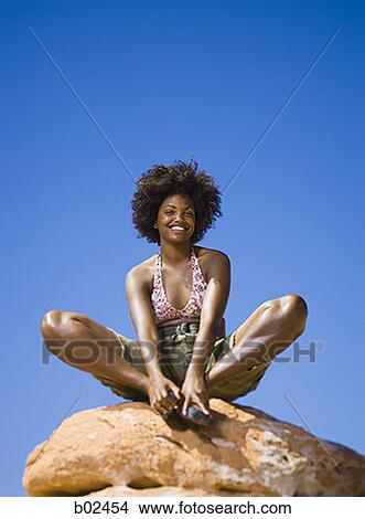 Low angle view of a young woman sitting on a rock View Large Photo Image Picture - Low angle view of a young woman sitting on a rock. Fotosearch