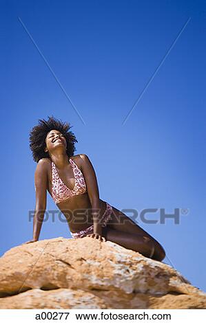 Low angle view of a young woman sitting on a rock View Large Photo Image Stock Photo - Low angle view of a young woman sitting on a rock. Fotosearch