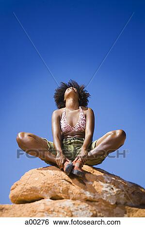 Stock Photograph - Low angle view of a young woman sitting on a rock. Fotosearch