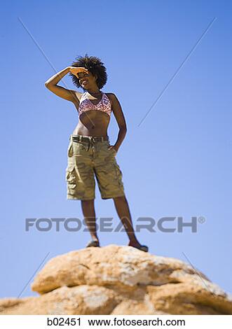Low angle view of a young woman standing on a rock View Large Photo Image Stock Image - Low angle view of a young woman standing on a rock. Fotosearch