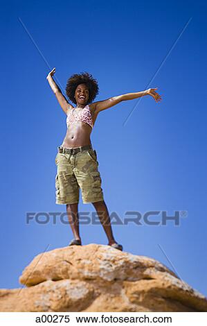 Low angle view of a young woman standing on a rock View Large Photo Image Stock Photography - Low angle view of a young woman standing on a rock. Fotosearch