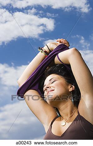 Low angle view of a young woman taking off her top View Large Photo Image Stock Image - Low angle view of a young woman taking off her top. Fotosearch