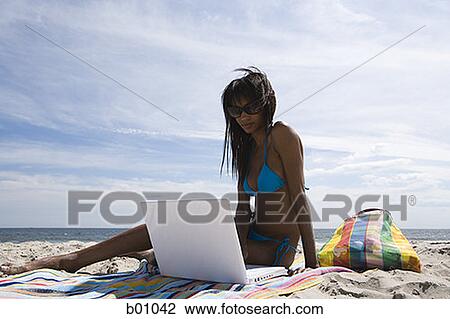 Low angle view of a young woman using a laptop on the beach View Large Photo Image Stock Image - Low angle view of a young woman using a laptop on the beach. Fotosearch