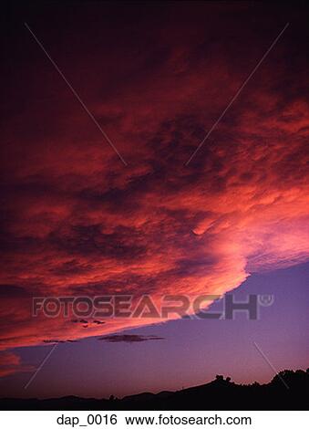 Stock Photograph - Low angle view of storm clouds over landscape at dusk. Fotosearch