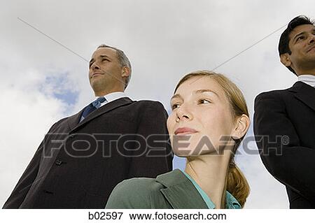 Stock Photo - Low angle view of two businessmen and a businesswoman smiling. Fotosearch