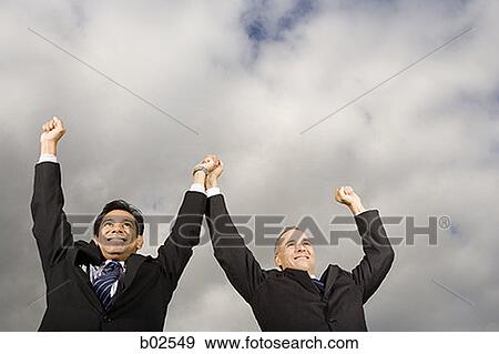 Stock Photo - Low angle view of two businessmen standing with their arm raised. Fotosearch