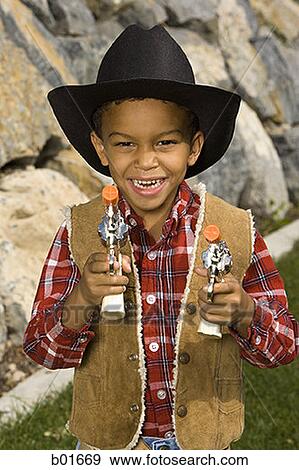 Portrait of a boy in a cowboy costume holding a toy gun View Large Photo Image Stock Photo - Portrait of a boy in a cowboy costume holding a toy gun. Fotosearch