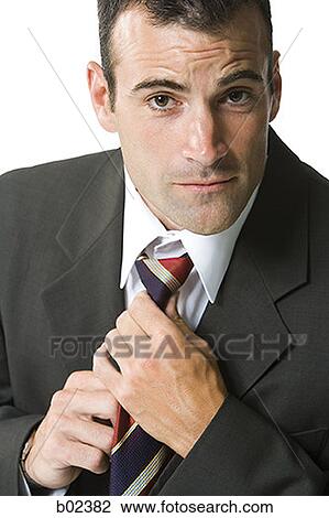 Stock Image - Portrait of a businessman adjusting his tie. Fotosearch