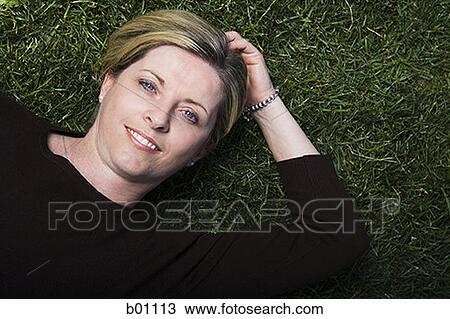 Stock Image - Portrait of a mature woman lying on a lawn. Fotosearch