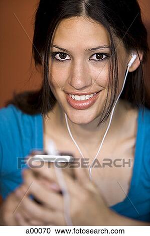 Stock Image - Portrait of a young Latin woman wearing headphones and listening to music. Fotosearch