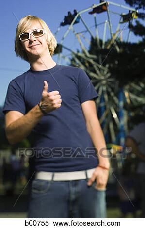 Stock Photography - Portrait of a young man showing a thumb's up sign in an amusement park. Fotosearch