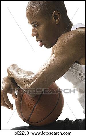 Stock Image - Portrait of a young man sitting and holding a basketball. Fotosearch