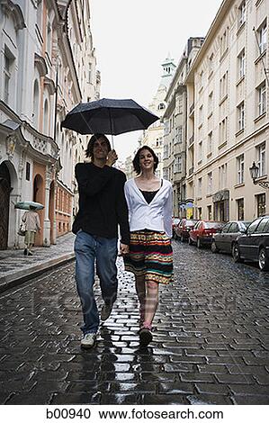 Stock Image - Portrait of a young man walking with a young woman under an umbrella. Fotosearch