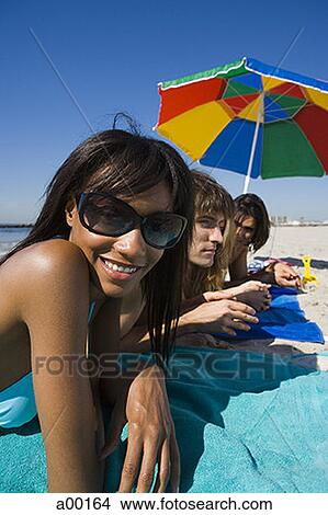 Picture - Portrait of a young woman lying on the beach with her friends. Fotosearch