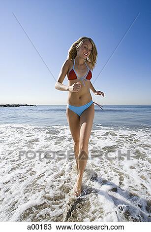Stock Image - Portrait of a young woman running on the beach. Fotosearch