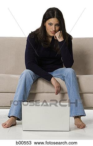 Portrait of a young woman sitting on a couch with a laptop in front of her View Large Photo Image Stock Image - Portrait of a young woman sitting on a couch with a laptop in front of her. Fotosearch