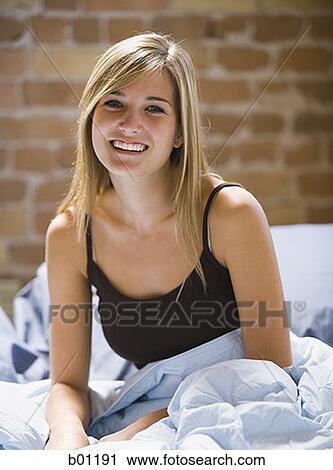 Portrait of a young woman sitting on a bed View Large Photo Image Stock Image - Portrait of a young woman sitting on a bed. Fotosearch