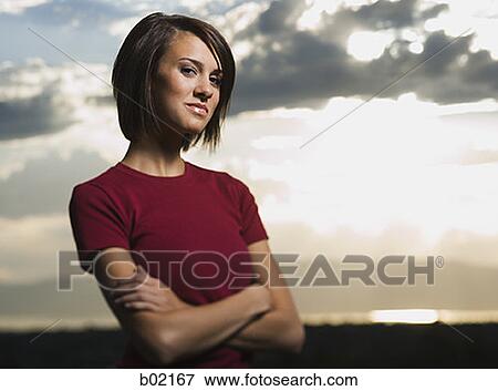 Stock Photo - Portrait of a young woman standing with her arms crossed. Fotosearch
