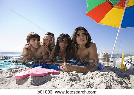 Stock Image - Portrait of four young people lying on the beach. Fotosearch