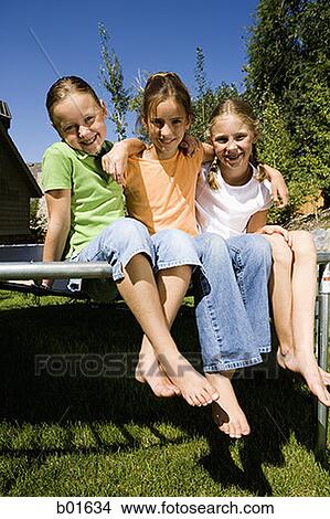 Picture - Portrait of three girls sitting on a trampoline. Fotosearch