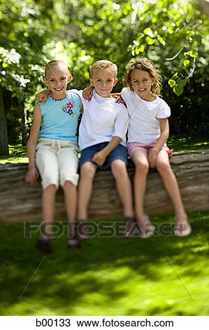 Portrait of two girls and a boy sitting on a tree trunk View Large Photo Image Stock Image - Portrait of two girls and a boy sitting on a tree trunk. Fotosearch
