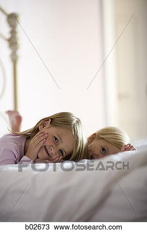 Stock Image - Portrait of two sisters lying on the bed. Fotosearch