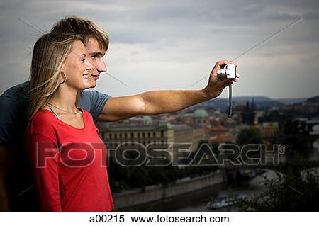 Stock Photography - Profile of a young man and a young woman taking a photograph of themselves. Fotosearch
