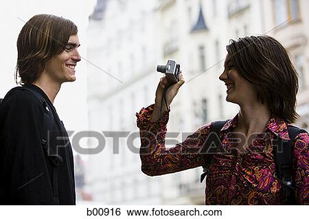 Profile of a young woman taking a young man's photograph View Large Photo Image Stock Photograph - Profile of a young woman taking a young man's photograph. Fotosearch