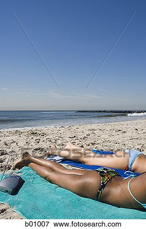 Stock Photo - Profile of two young women sunbathing on the beach. Fotosearch