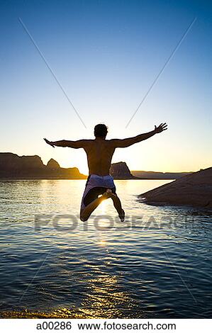 Rear view of a young man jumping into a lake View Large Photo Image Stock Photograph - Rear view of a young man jumping into a lake. Fotosearch