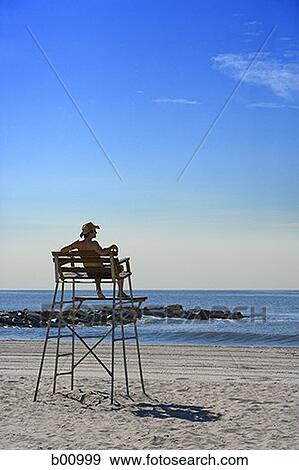 Stock Photo - Rear view of a young man sitting on a lifeguard chair. Fotosearch
