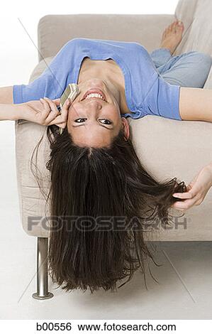 Rear view of a young woman lying on a couch and talking on a mobile phone View Large Photo Image Stock Photograph - Rear view of a young woman lying on a couch and talking on a mobile phone. Fotosearch