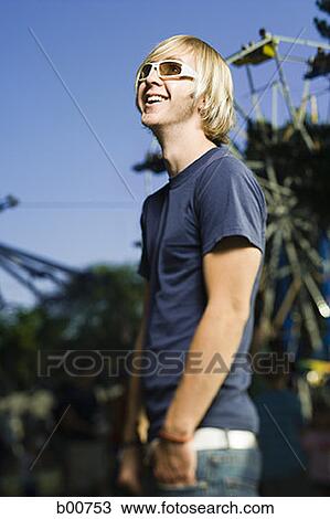 Stock Image - Side profile of a young man standing in an amusement park. Fotosearch
