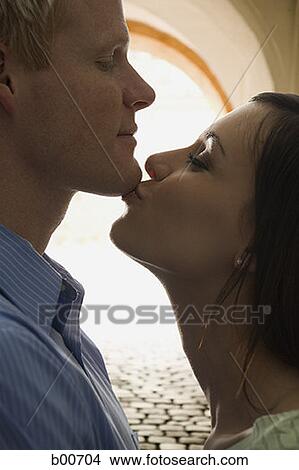 Picture - Side profile of a young woman kissing a young man on his chin. Fotosearch