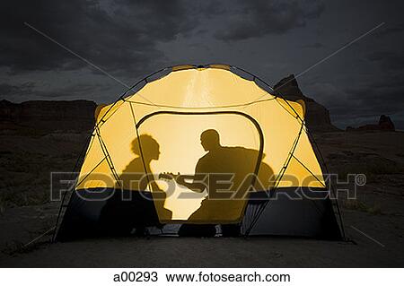 Stock Image - Silhouette of a couple sitting inside a tent. Fotosearch
