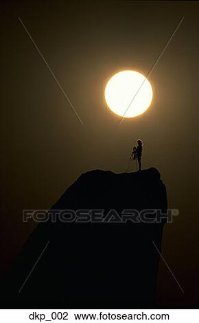 Stock Image - Silhouette of a couple standing on the mountain peak. Fotosearch