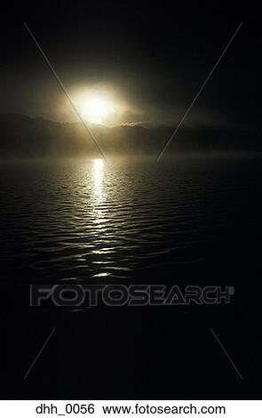Sun setting behind dark mountains and water View Large Photo Image Stock Photograph - Sun setting behind dark mountains and water. Fotosearch