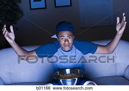 Stock Photograph - Teenage boy sitting in a couch, watching TV. Fotosearch