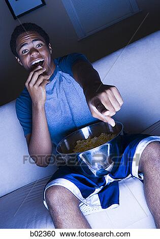 Teenage boy watching television and eating popcorn View Large Photo Image Stock Image - Teenage boy watching television and eating popcorn. Fotosearch