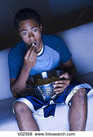 Teenage boy watching television and eating popcorn View Large Photo Image Stock Photo - Teenage boy watching television and eating popcorn. Fotosearch