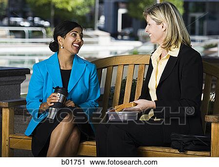 Two businesswomen sitting on a bench and talking View Large Photo Image Stock Image - Two businesswomen sitting on a bench and talking. Fotosearch