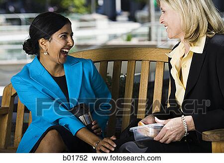 Two businesswomen sitting on a bench and talking View Large Photo Image Stock Image - Two businesswomen sitting on a bench and talking. Fotosearch