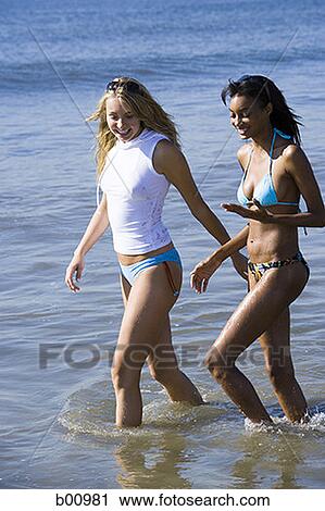 Stock Image - Two young women wading in the water on the beach. Fotosearch