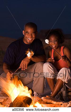 Stock Photograph - Young couple sitting by a campfire. Fotosearch