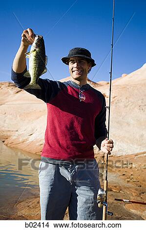 Young man holding a fish with a fishing pole View Large Photo Image Picture - Young man holding a fish with a fishing pole. Fotosearch