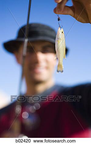 Young man holding a fishing bait with a fishing pole View Large Photo Image Stock Image - Young man holding a fishing bait with a fishing pole. Fotosearch